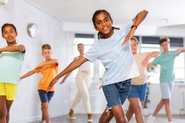 .African male youngster engaged shake leg in fitness studio with friends, young children and teacher good mood actively move and dance at choreography lesson in background