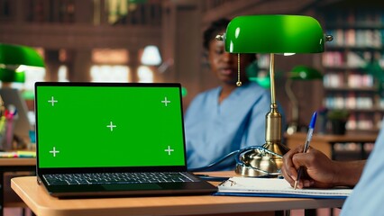 African american male nurse studies anatomy textbooks next to green screen in a university library, using academic database for a successful medical career. Med school. Camera B.