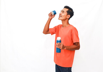 Hydrated young man enjoying a refreshing drink from his blue thermal flask on a bright day