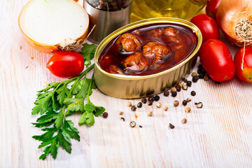 Seafood appetizer. Canned variegated scallops in salsa in open tin on wooden table with greens, tomatoes, oil