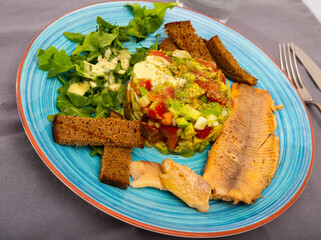 Baked trout fillets with vegetable garnish of guacamole salad, fresh arugula and toasted rye bread