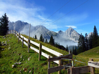 A fence of a cattle pen on a mountain summer pasture in perspective. Mountains and blue sky behind.