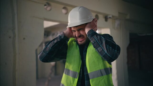 Caucasian builder worker man guy male handyman engineer architect in hardhat employee closing ears with hands industrial loud explosion in construction factory hiding from demolition building noise