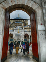 Tourists entering S&uuml;leymaniye Mosque courtyard in Istanbul, Turkey, through a large carved wooden door