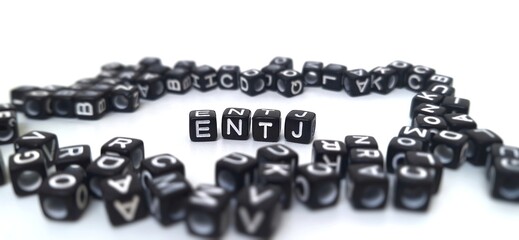 Scattered black plastic cubes, focus on the letters ENTJ in the center. The foreground and background are blurred. ENTJ is one of the 16 personality types identified by the MBTI test.