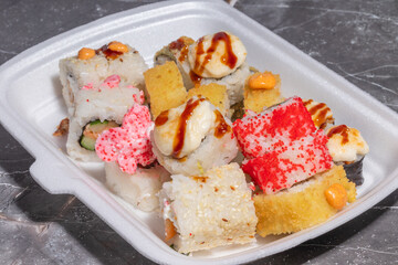 Mixed sushi platter with tempura-fried rolls and colorful toppings, presented in a takeout container.