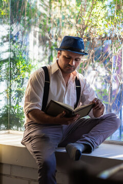 latino mafioso man sitting by window reading a book