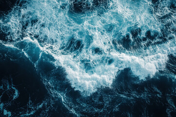 Blue and white ocean waves crashing against rocky cliffs under a clear sky with a lone surfer riding a large wave in the distance.