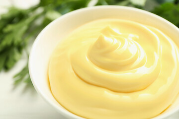 Delicious mayonnaise sauce in bowl and parsley on white table, closeup