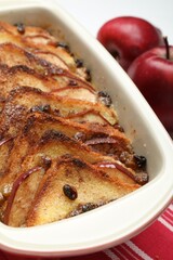 Delicious bread pudding in baking dish and fresh apples on table, closeup