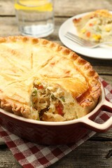 Tasty homemade pie with chicken and vegetables in baking dish on wooden table, closeup