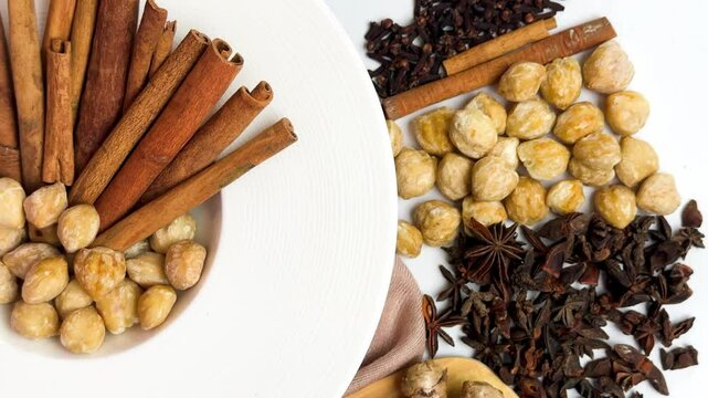 Top view of assorted traditional spices used in Indonesian and Asian cooking, including ginger, turmeric, galangal, cinnamon sticks, cloves, corriander seedsand candlenuts on white backgrounds.