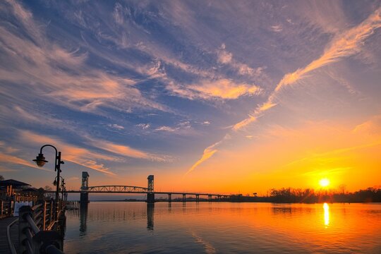 A beautiful sunset landscape of the Cape Fear Memorial Bridge from the Wilmington Riverwalk under a cloudy sky in North Carolina.
