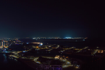 Aerial view of Abu Dhabi at night, showcasing the city's illuminated skyline, modern skyscrapers, and roads glowing under the night sky.