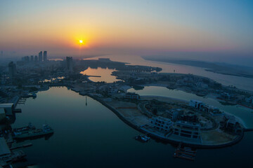Aerial view of Abu Dhabi in the morning light, as the rising sun casts a golden glow over the city's modern skyline.