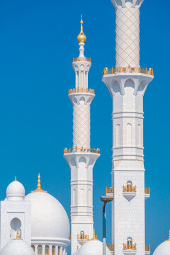 Close-up of the Sheikh Zayed Grand Mosque, showcasing its intricate white marble domes and elegant architectural details against a vivid blue sky. 