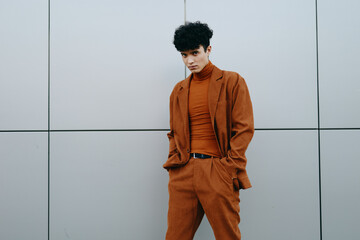 Stylish young man in modern rust colored outfit against a gray wall