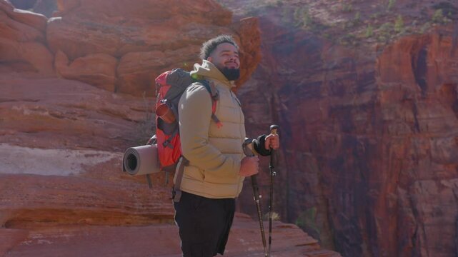 An African American male adventurer takes a moment to pause and appreciate the breathtaking views of the impressive Zion National Park while engaging in a fulfilling backpacking hike with his gear
