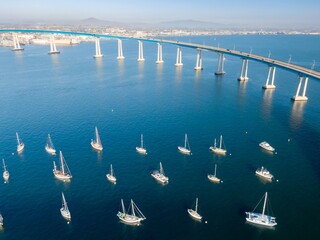 Aerial view of sailboats anchored in San Diego Bay, USA, beneath the Coronado Bridge. The boats are...