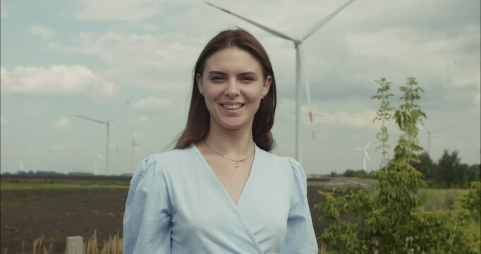 Young woman smiling near wind turbines in agricultural field