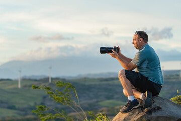 Caucasian man photographing landscape from mountain at sunset