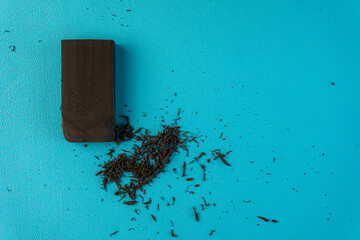 An overhead shot displays a dark eraser alongside its residue on a clean turquoise backdrop.
