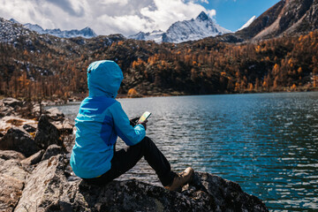 Woman hiker using mobile phone on autumn high altitude lakeside