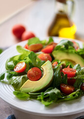 Fresh Mixed Green Salad with Avocado, Tomatoes, and Olive Oil in Natural Light on White Plate