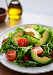 Fresh Mixed Green Salad with Avocado, Tomatoes, and Olive Oil in Natural Light on White Plate