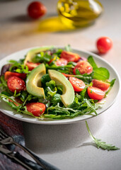 Fresh Mixed Green Salad with Avocado, Tomatoes, and Olive Oil in Natural Light on White Plate
