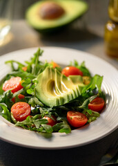 Fresh Mixed Green Salad with Avocado, Tomatoes, and Olive Oil in Natural Light on White Plate