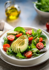 Fresh Mixed Green Salad with Avocado, Tomatoes, and Olive Oil in Natural Light on White Plate