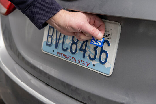 Hand placing registration tab 2026 on the license plate. DMV sticker