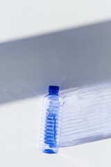 Transparent plastic bottles with blue caps and sun shadows on light background. Top view Water...