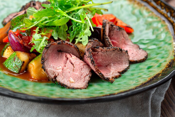 Warm salad with roast beef and stewed vegetables on a plate. Hearty salad with beef and herbs, close up