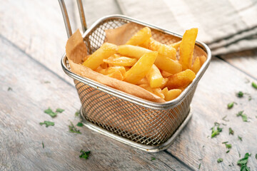 Crunchy fried potato wedges in an elegant metal basket with parchment, topped with fresh greenery, placed on a wooden surface. Perfect for a savory dinner or quick appetizer