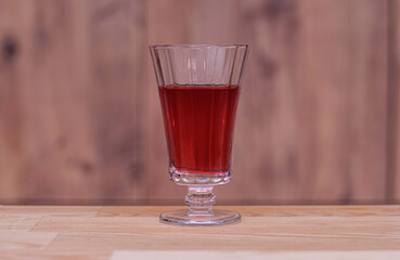 Red drink in an elegant glass goblet. Glass filled with a deep red beverage stands gracefully on a wooden table against a blurred wooden background. Selectice focus.