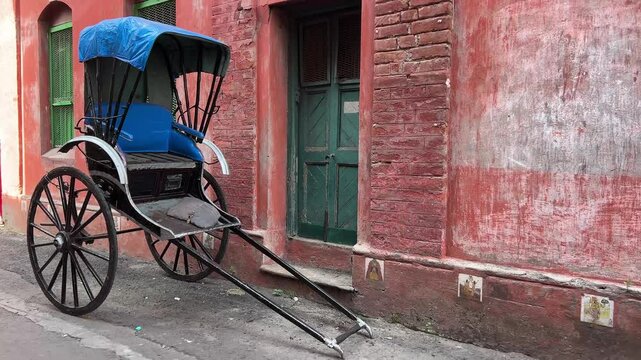 Profile view of hand pulled vintage rickshaw of Kolkata near a red color house with green vintage gate.