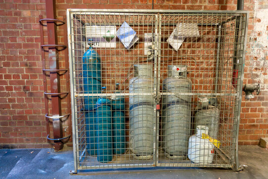 A metal cage enclosure safely stores various gas cylinders and tanks, providing secure storage for hazardous materials in a locked wire mesh cabinet and ensuring proper containment practices.