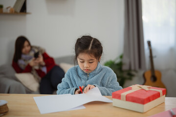 Naklejka premium Asian Child Engaged in Creative Activity with Paper and Scissors While Parent Relaxes in Background at Home