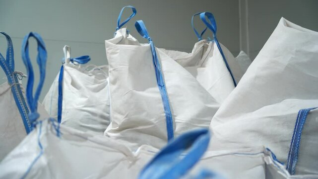 Large plastic bags with loop handles filled with recyclable plastic materials. Sacks in warehouse include chemicals and fertilizers closeup