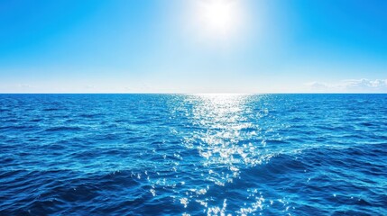 Fototapeta premium Sunlight sparkles on the calm ocean waves under a clear blue sky, creating a serene atmosphere. The scene captures the beauty of nature's tranquility at midday