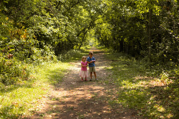 Fototapeta premium Two young children walking on a sunlit forest path in summertime