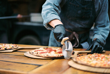 A chef in gloves slicing fresh wood-fired pizzas on a rustic tab