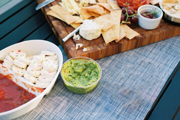 A charcuterie board with cheese, crackers, guacamole, and pinwhe
