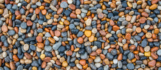 Colorful pebbles background featuring smooth rocks in shades of gray, black, orange, and white, creating natural texture for design and decoration