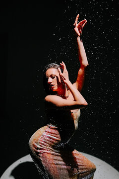 Dancer performing under dramatic lighting and water droplets in a creative dance studio setting