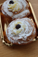 Two Italian fried Zeppole on a golden cardboard tray for St. Joseph (Father’s day)