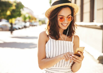 Portrait of happy smiling woman in summer hipster clothes. Female listening music on her headphones from smartphone in the street in a summer sunny day