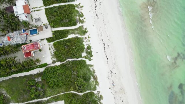 Beachfront aerial view with tropical villas, sandy paths, and turquoise waters in Cuyo, Mexico